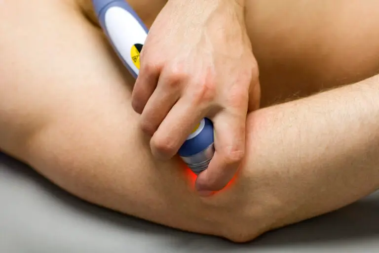 A therapist using a cold laser therapy to treat a patient's elbow, with the patient's arm resting on a treatment table.