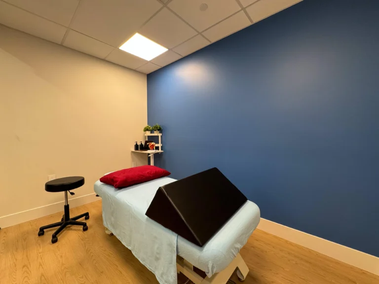 Massage therapy room featuring a comfortable treatment table, a stool, and a desk with premium massage oils, arranged for a relaxing and professional therapeutic environment.