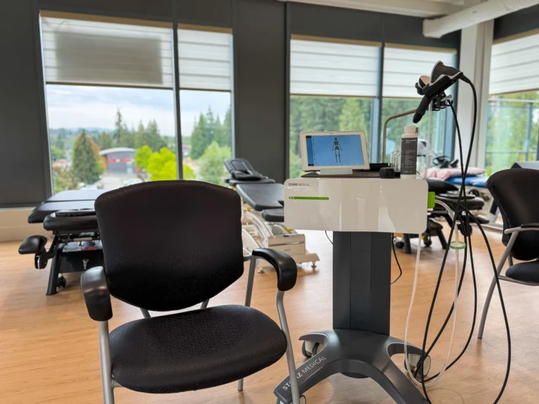 Therapy setup with a comfortable chair, a shockwave machine for physical therapy, and a tablet on the shockwave machine, used for treatment monitoring and control.